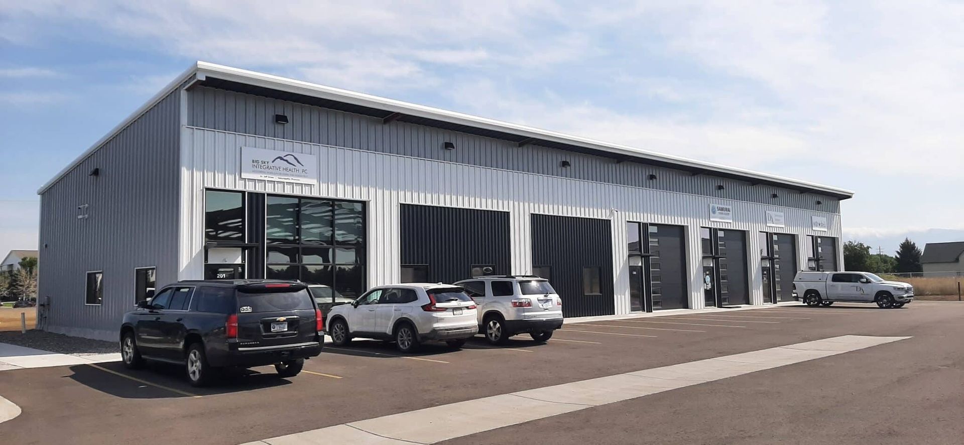 A large, metal building with several garage doors and parked vehicles in front.