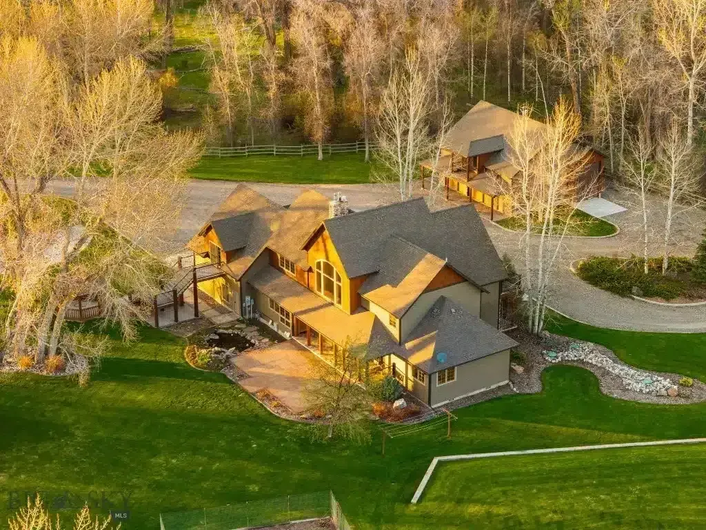 Aerial view of a large house with a detached structure, surrounded by trees and green lawn.