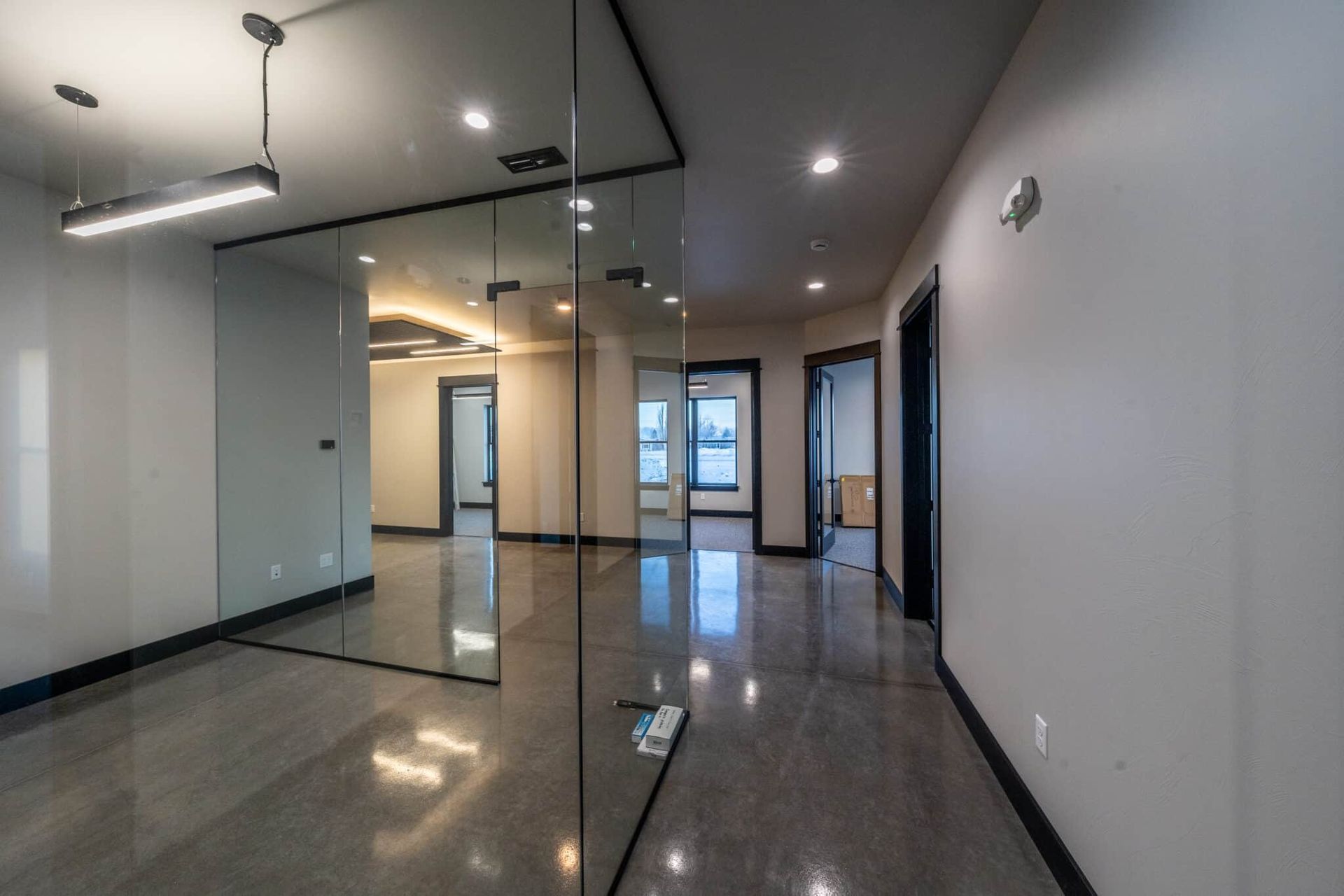 Modern office interior with glass walls, polished concrete floor, gray walls, and recessed lighting.