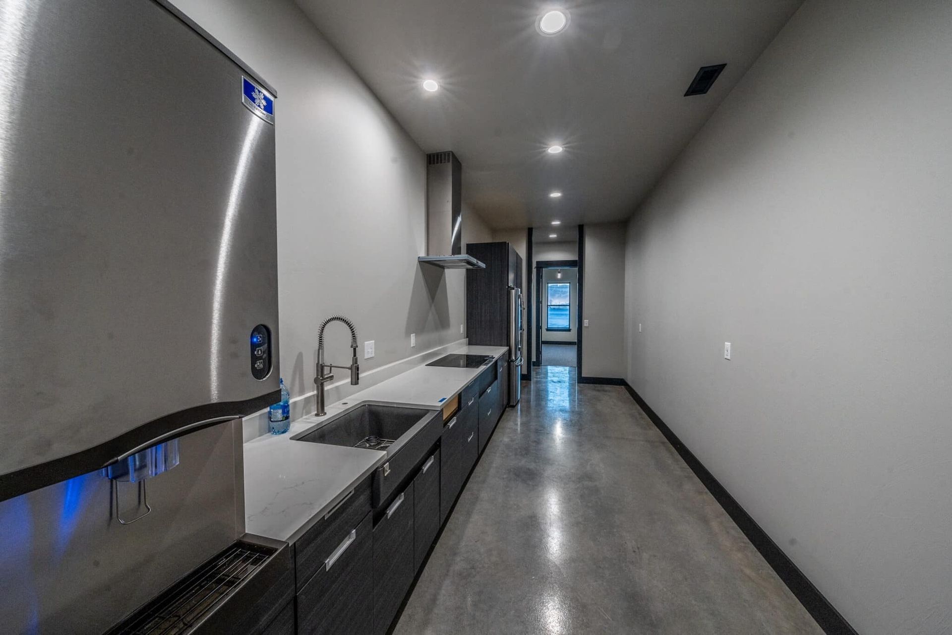 Long, narrow kitchen with gray cabinets, countertop, and concrete floor. Stainless steel appliances.