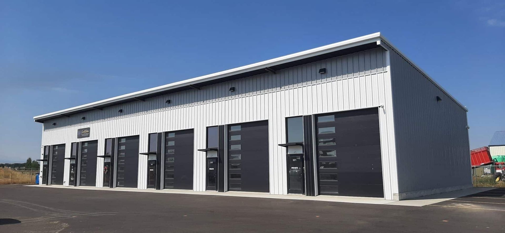 Gray metal industrial building with black garage doors against a blue sky.