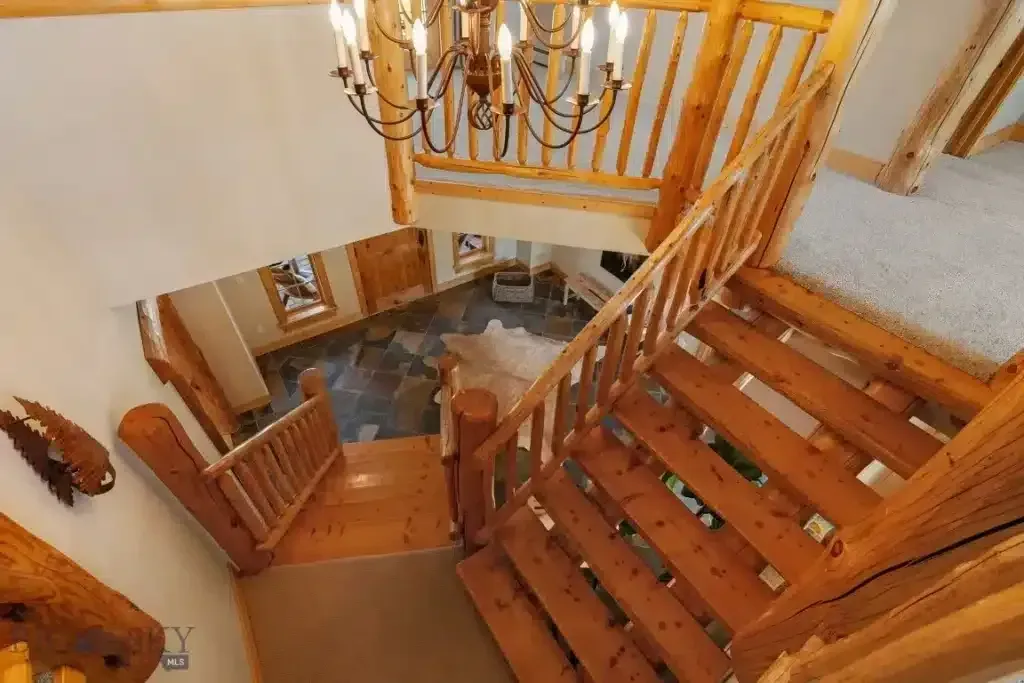 Wooden staircase in a cabin, viewed from above, with a chandelier and natural light.