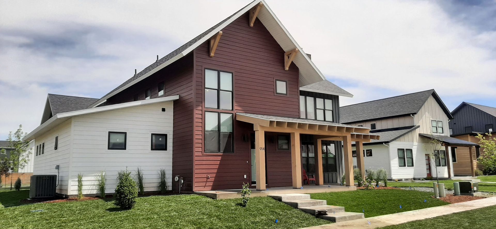 Modern house with red and white siding, front porch, and green lawn under a blue sky.
