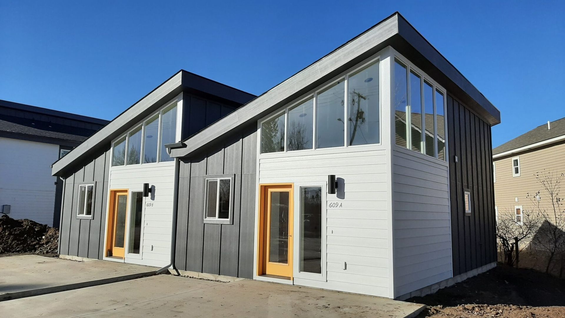 Modern duplex with gray and white siding, angled roof, large windows, and yellow doors.