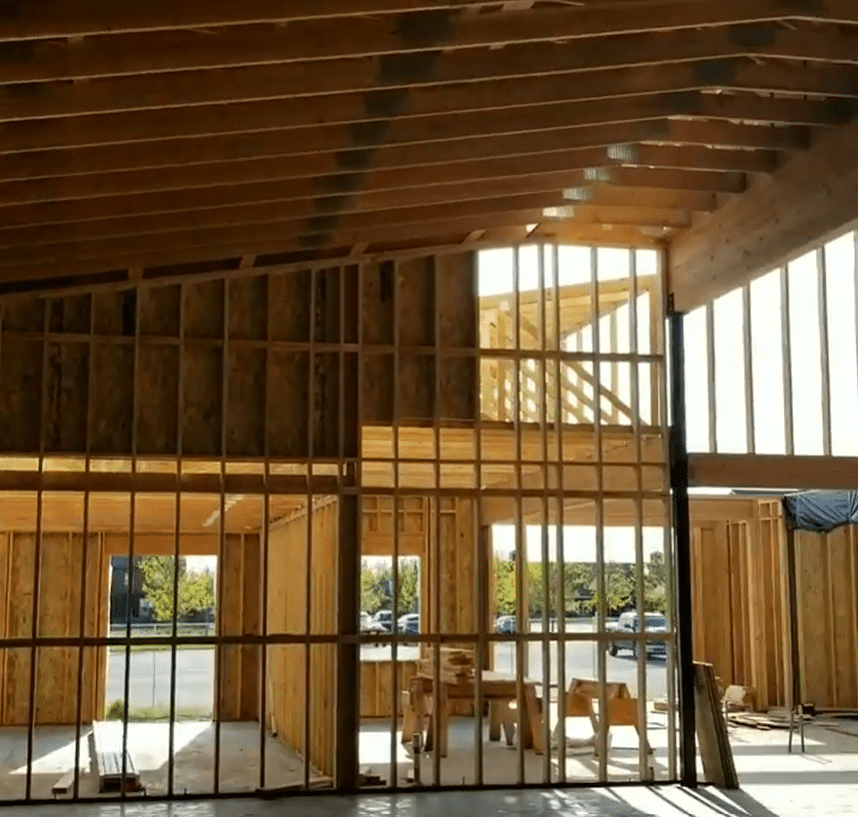 Interior view of a building under construction, showing wooden frames and beams. Sunlight streams through openings.