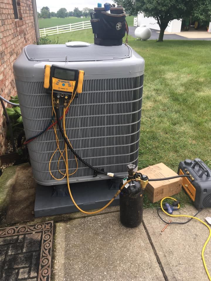 An air conditioner is being serviced on a sidewalk next to a brick building.