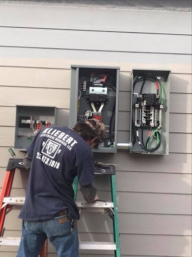 A man is standing on a ladder working on an electrical box.