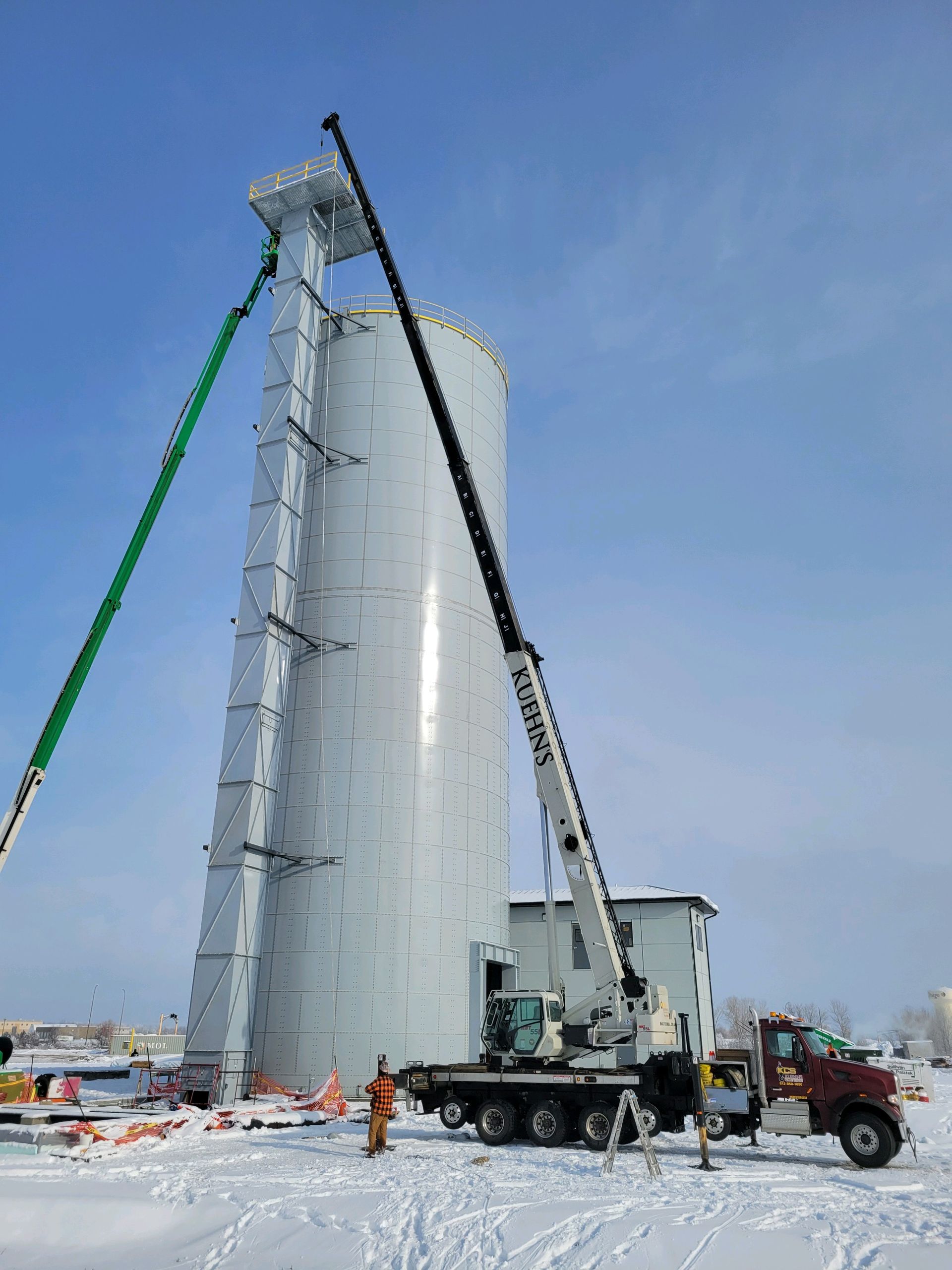 A crane is lifting a large silo in the snow.