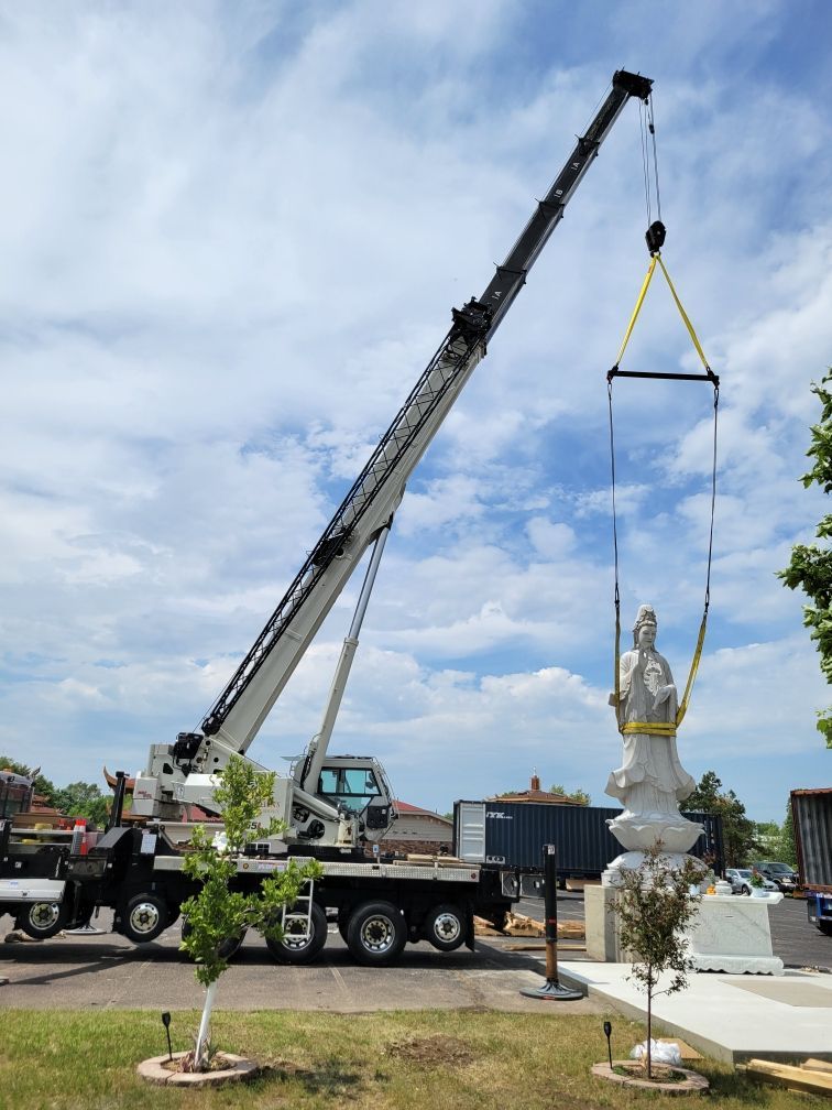 A truck with a crane attached to it is lifting a statue.