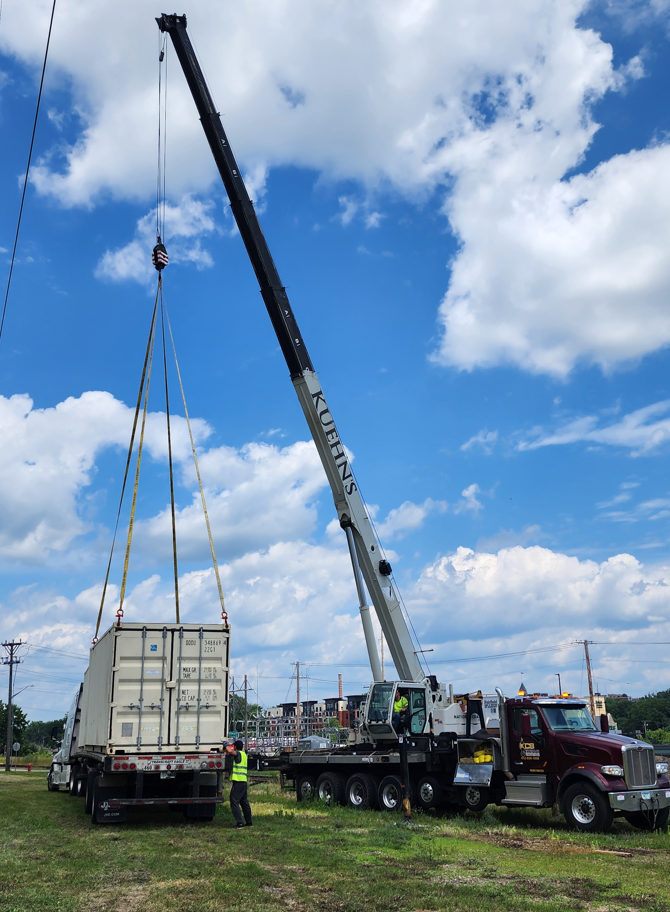 A large crane is lifting a shipping container into a truck