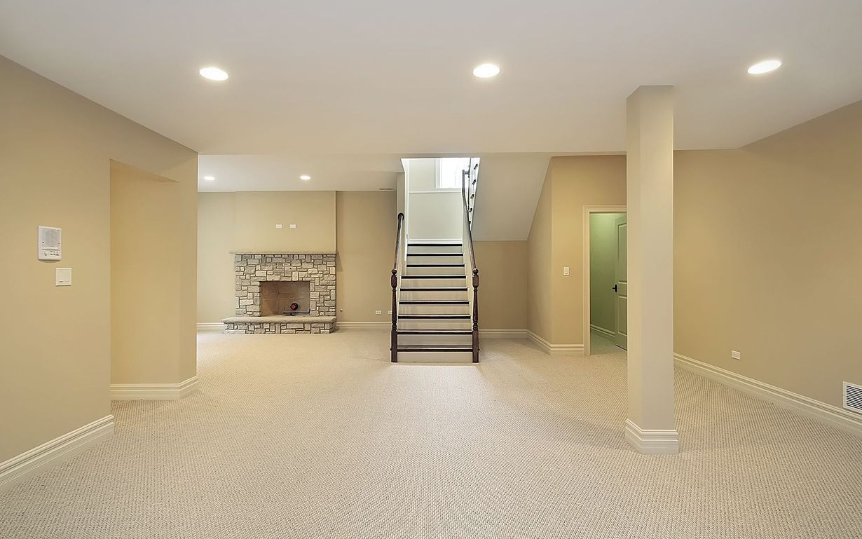 An empty basement with a fireplace and stairs leading up to the second floor.
