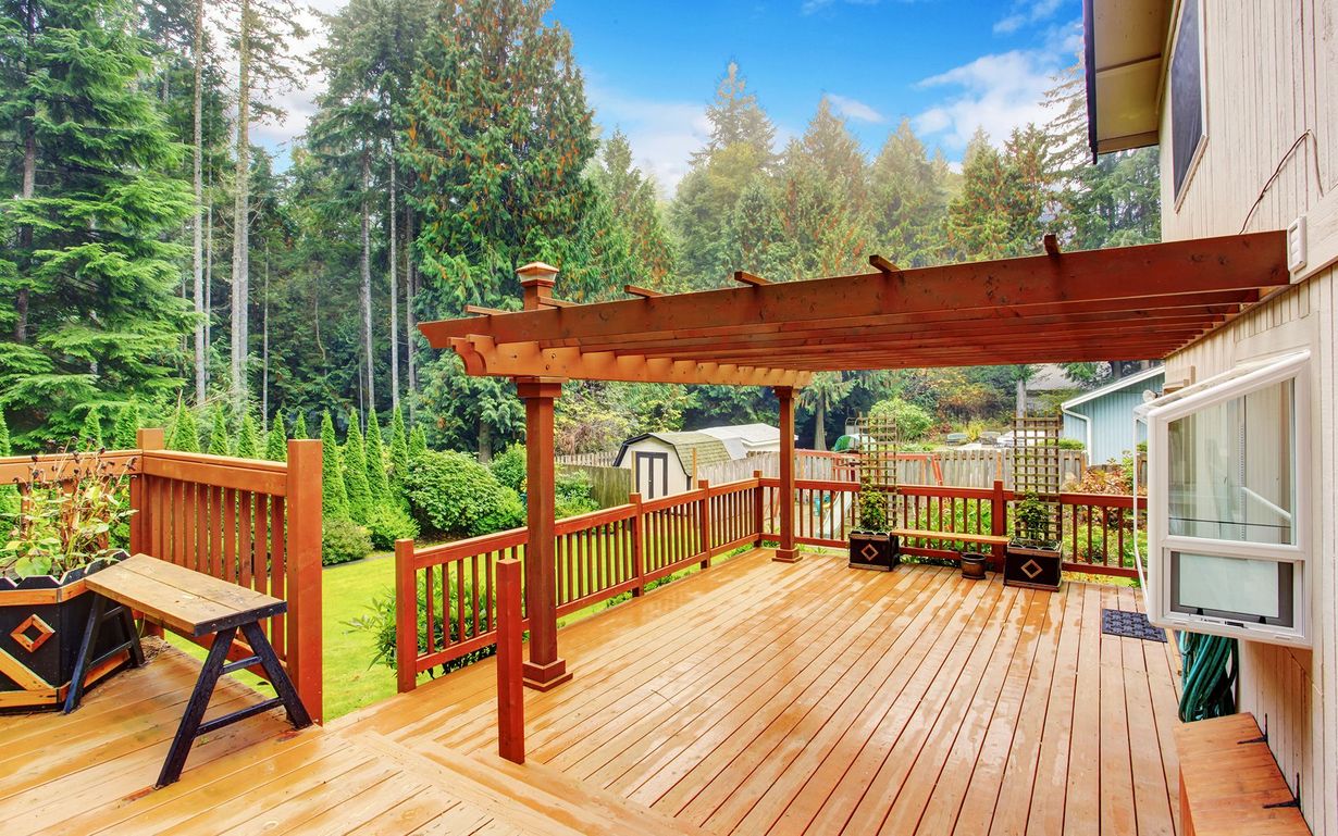 A large wooden deck with a pergola and a bench.