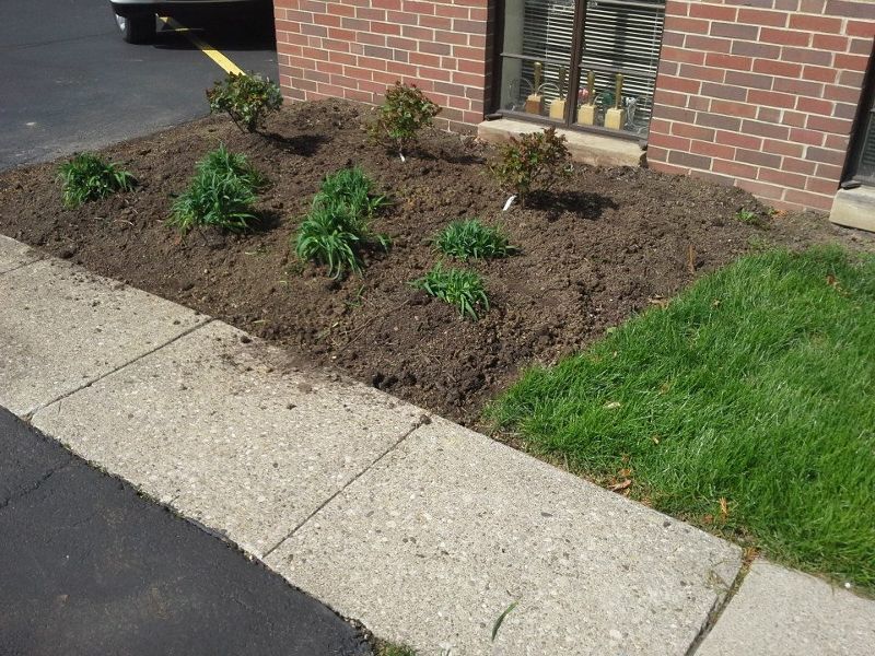 A brick building with a sidewalk and a garden in front of it