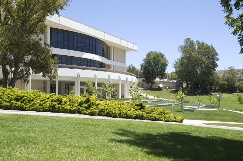 A large white building with a lot of windows is surrounded by trees and grass.