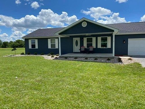A blue house with a white garage door is sitting on top of a lush green field.