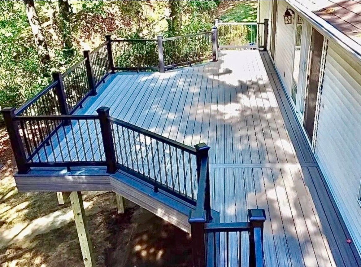 Elevated deck with black railing and light gray composite decking, connected to a beige house, surrounded by trees.