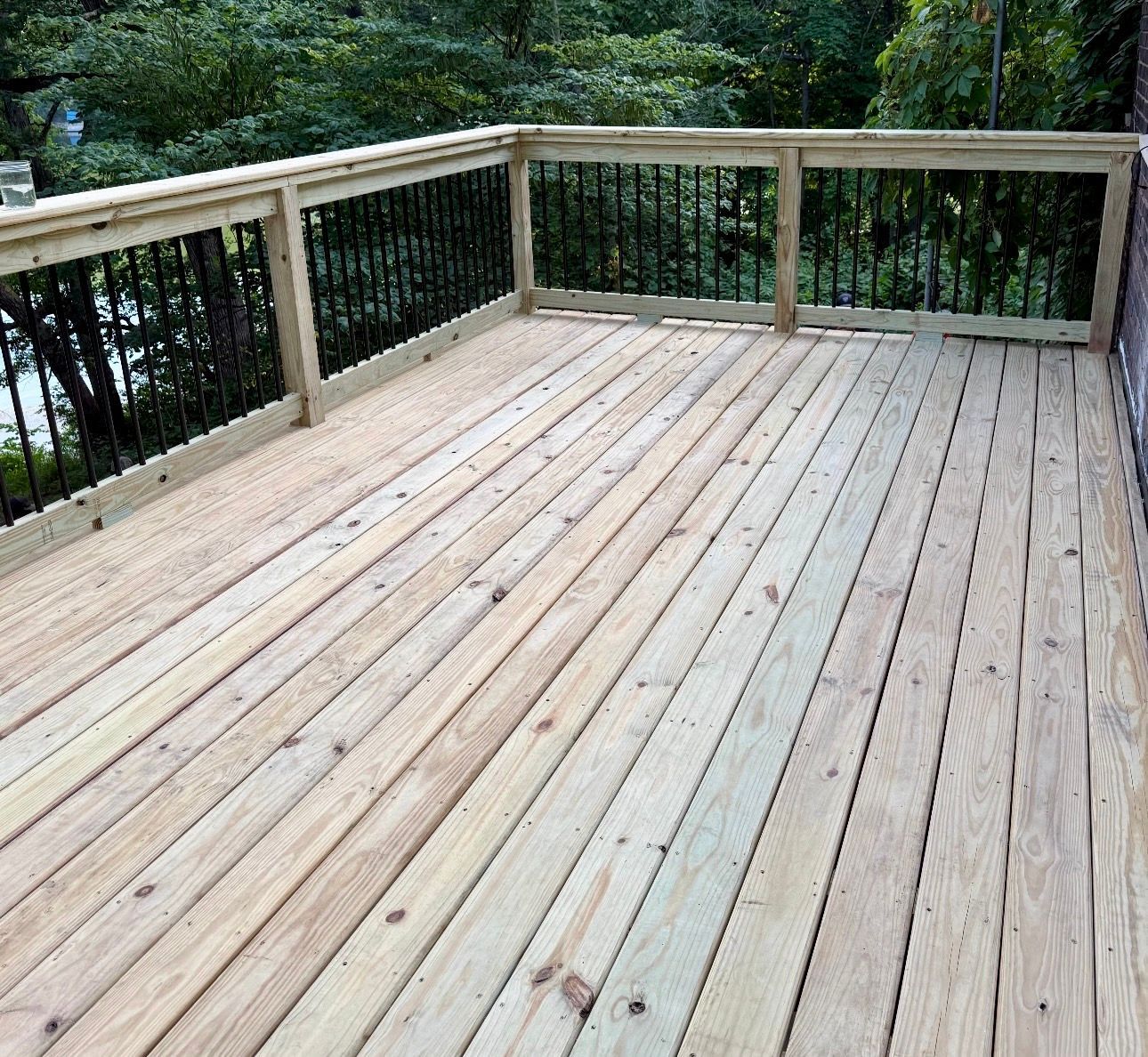 Wooden deck with black metal railing, surrounded by trees.