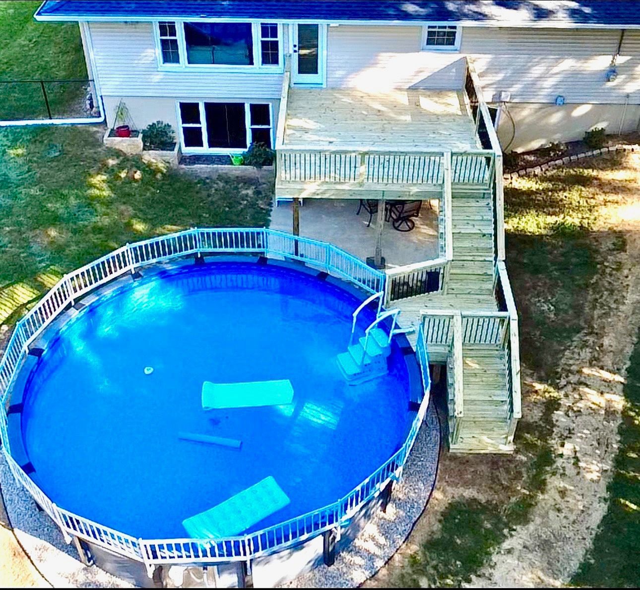 Above-ground pool with deck and stairs, backyard setting. Blue water, green grass, beige house.