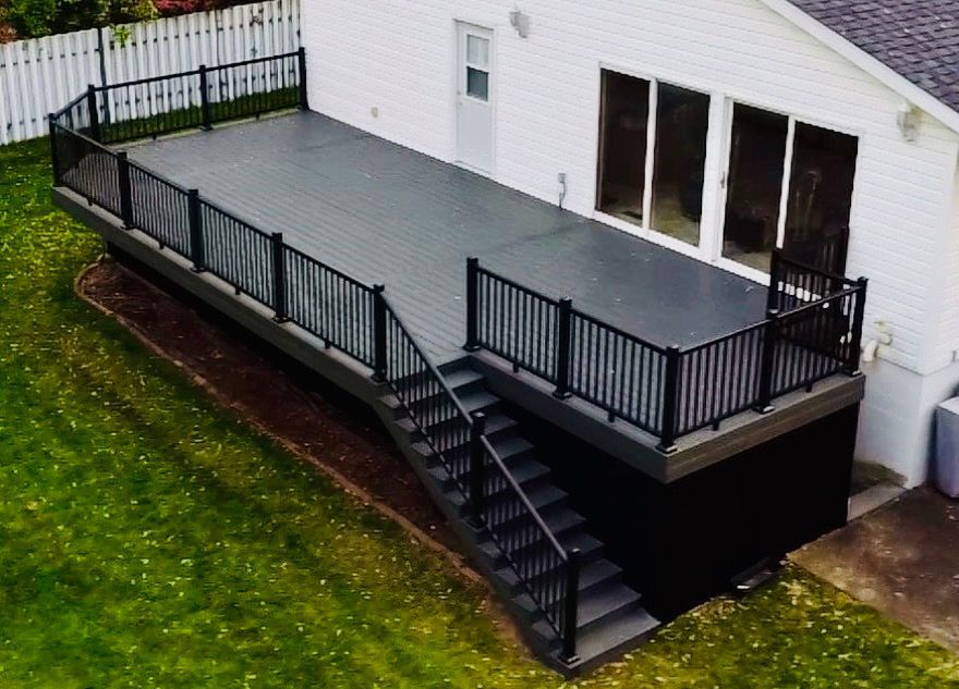 Composite deck with black railing and stairs attached to a white house, set in a grassy yard.