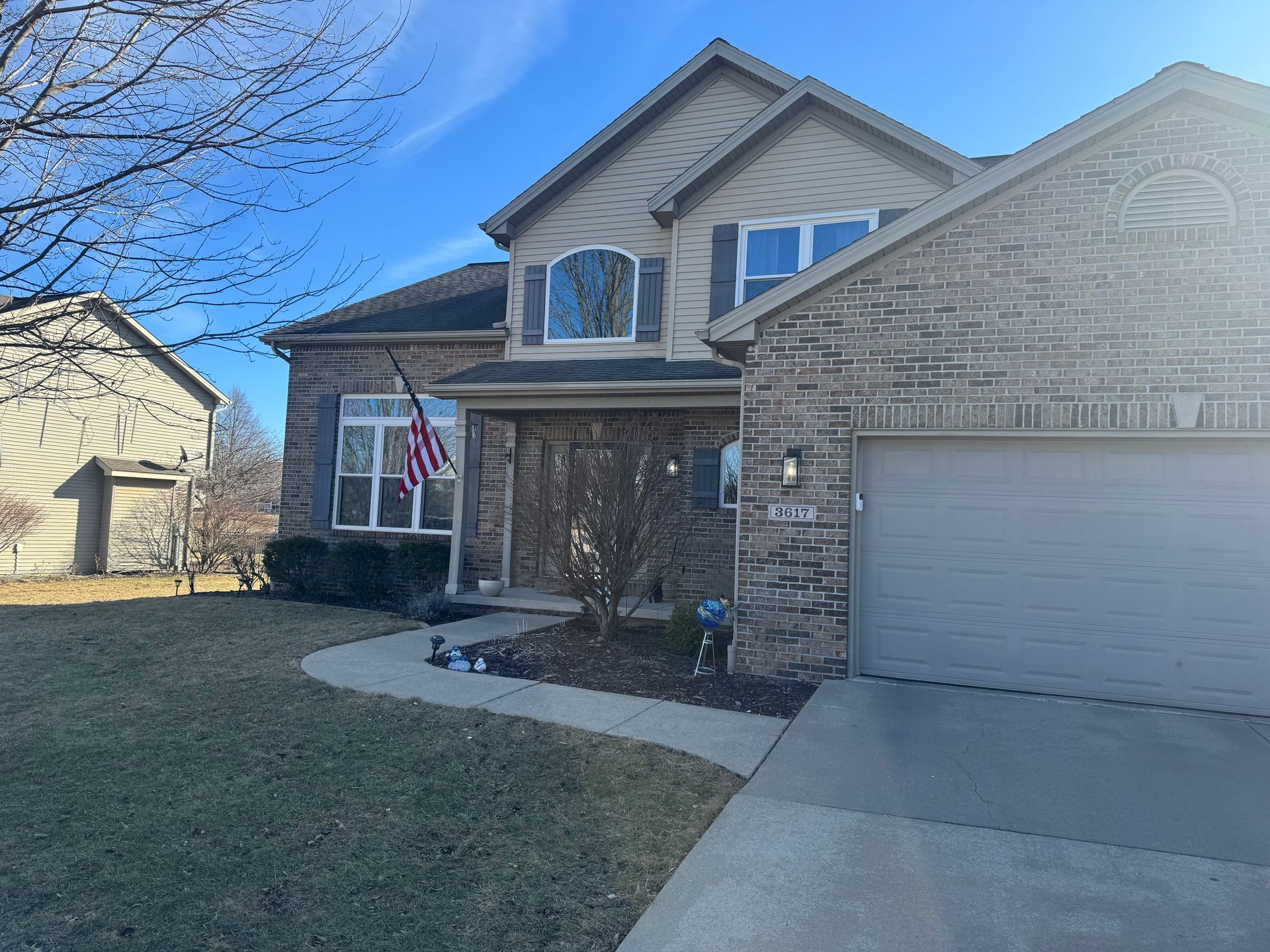 Two-story house with brick and siding, flag, and a driveway on a sunny day.