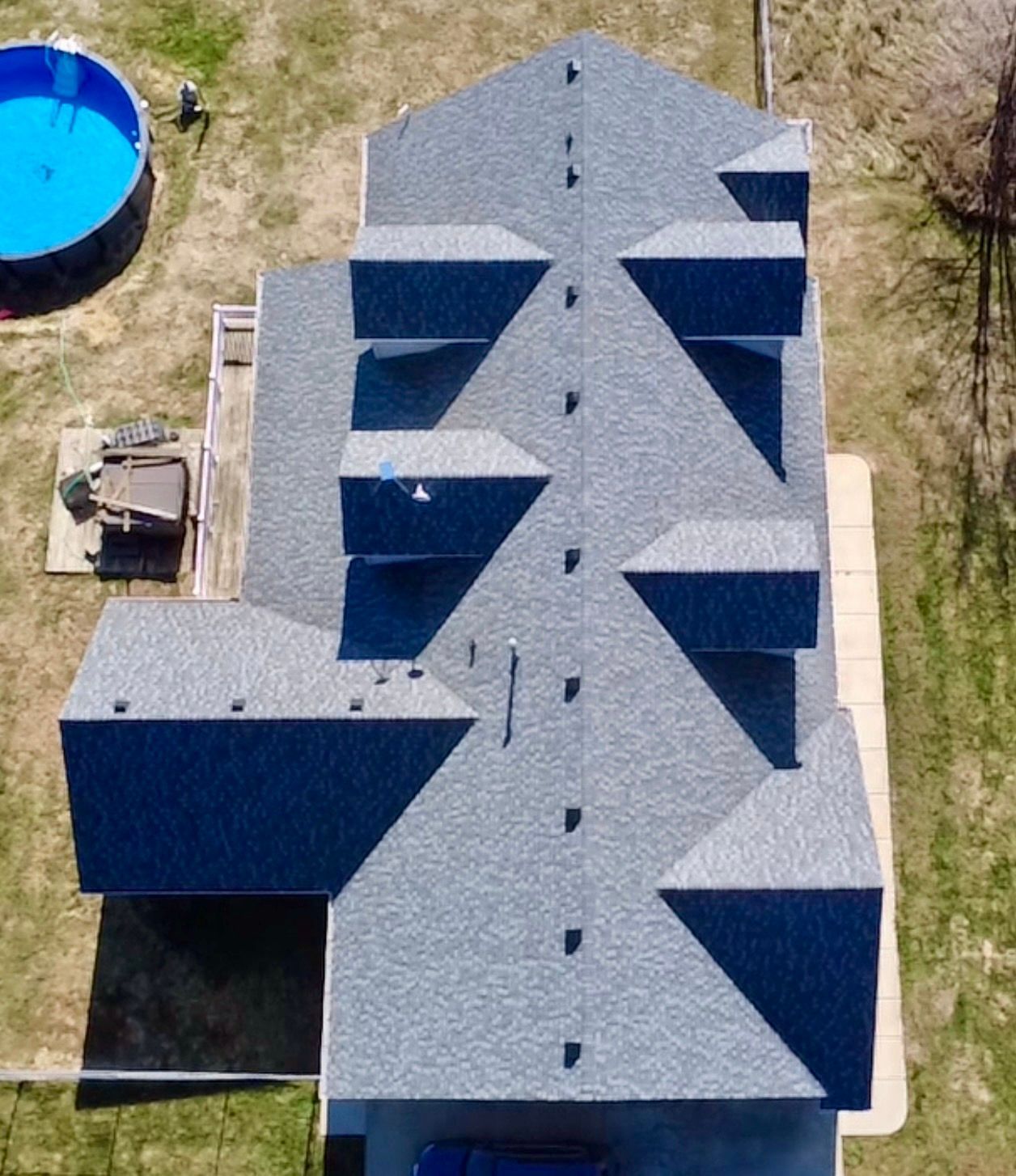 Overhead view of a house with a complex gray roof, a blue pool, and a lawn.
