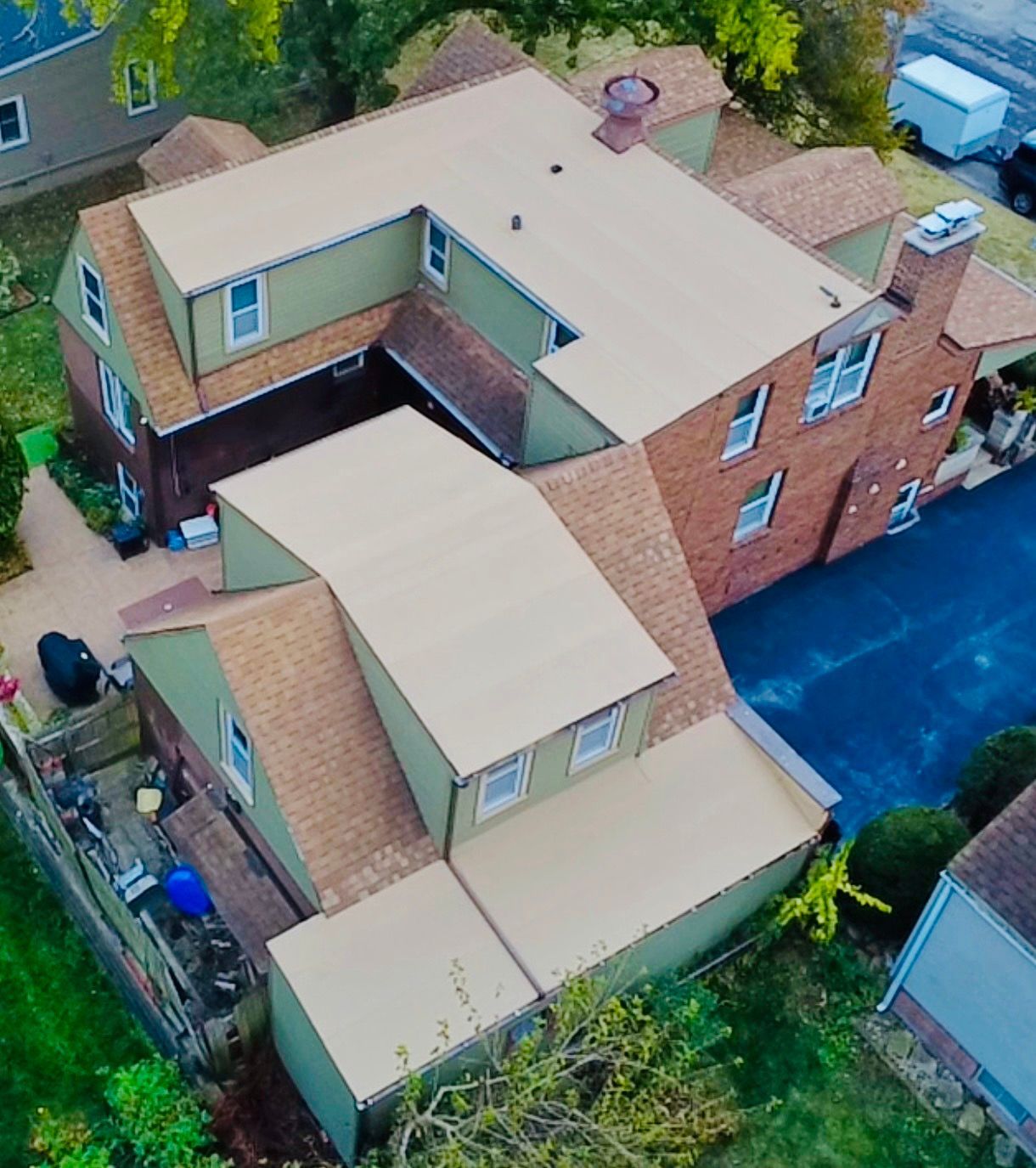 Aerial view of a multi-sectioned house with a complex roof structure, green and brown walls, and a driveway.