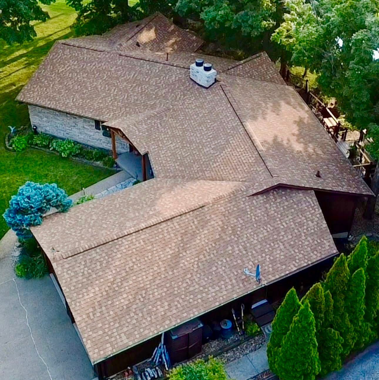 Brown roofed house surrounded by green trees and lawn, seen from above.