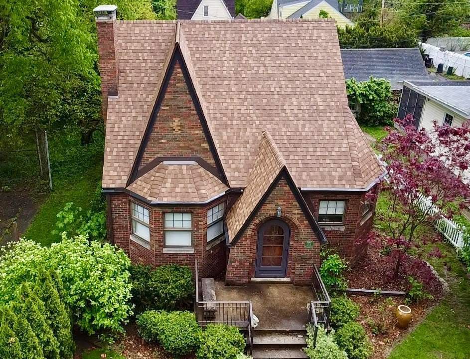 Brick Tudor-style house with brown roof and landscaping. Exterior shot, sunny day.