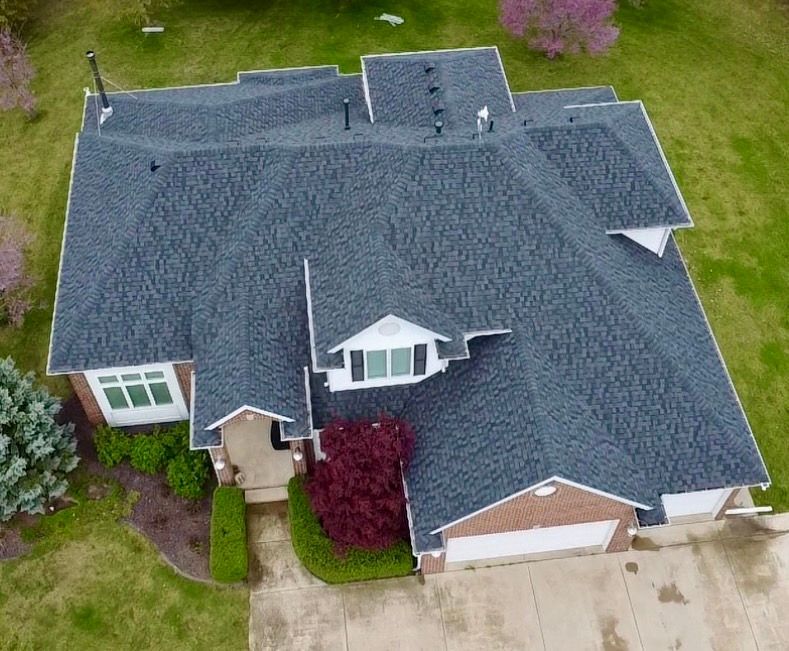 Overhead view of a house with a dark gray shingled roof, red brick facade, and green lawn.