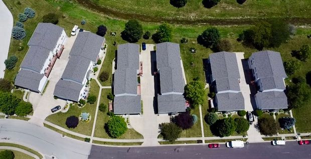 An aerial view of six townhome buildings arranged in pairs, separated by driveways, surrounded by lawns and trees.