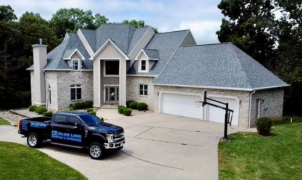 A black service truck parked in the driveway of a large, two-story brick suburban home with a three-car garage.