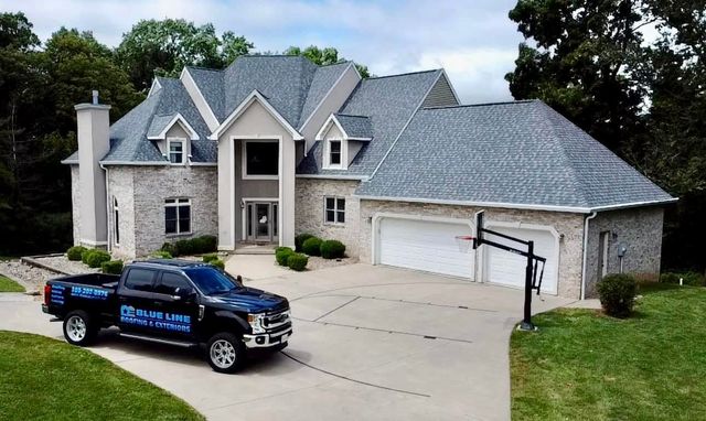 A black service truck parked in the driveway of a large, two-story brick suburban home with a three-car garage.
