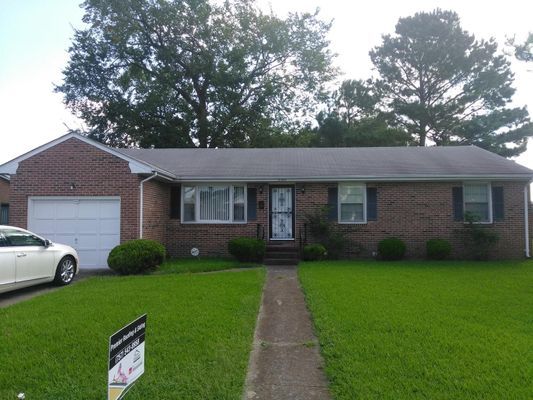 Brick ranch-style house with green lawn, driveway, and garage. A