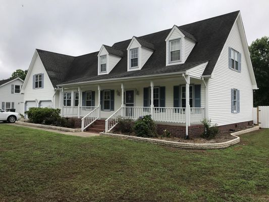 White house with a porch, dormer windows, and blue shutters; overcast day.