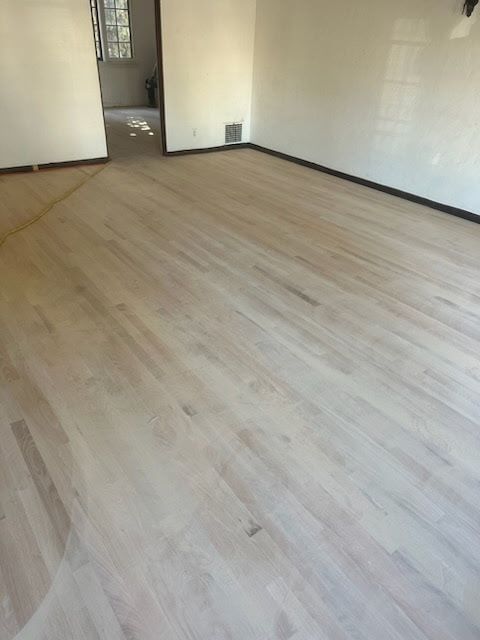 A room featuring newly sanded, light-toned hardwood flooring leading to an open doorway.