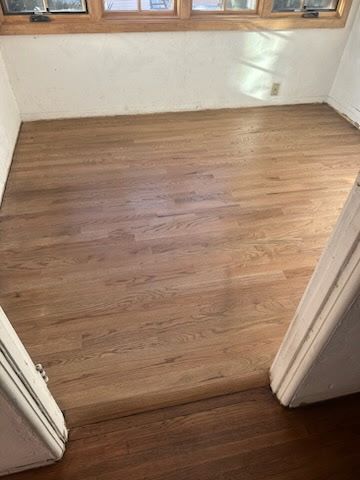A transition between a dark hardwood floor and a newly installed, lighter wood floor in a room with windows.