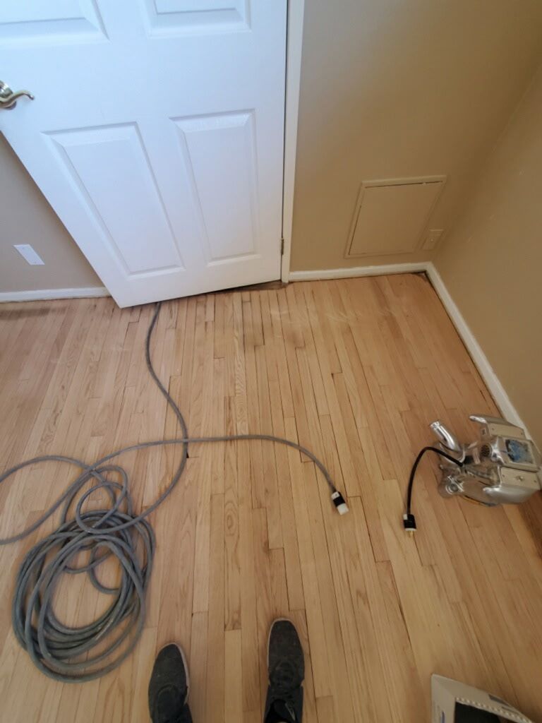 A room with light wood floors, a white door, and a coiled grey power cord laying on the ground near a machine.