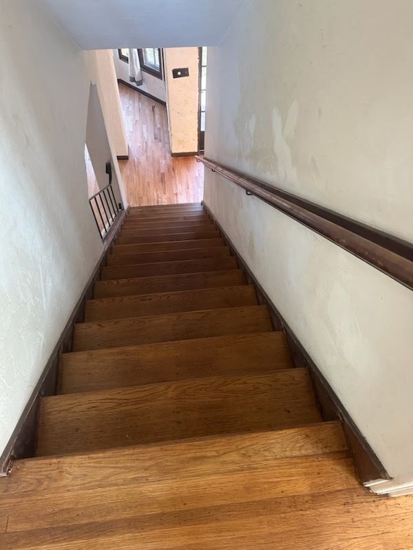 A steep wooden staircase leads down into a hallway with hardwood floors and a wooden handrail on the right wall.