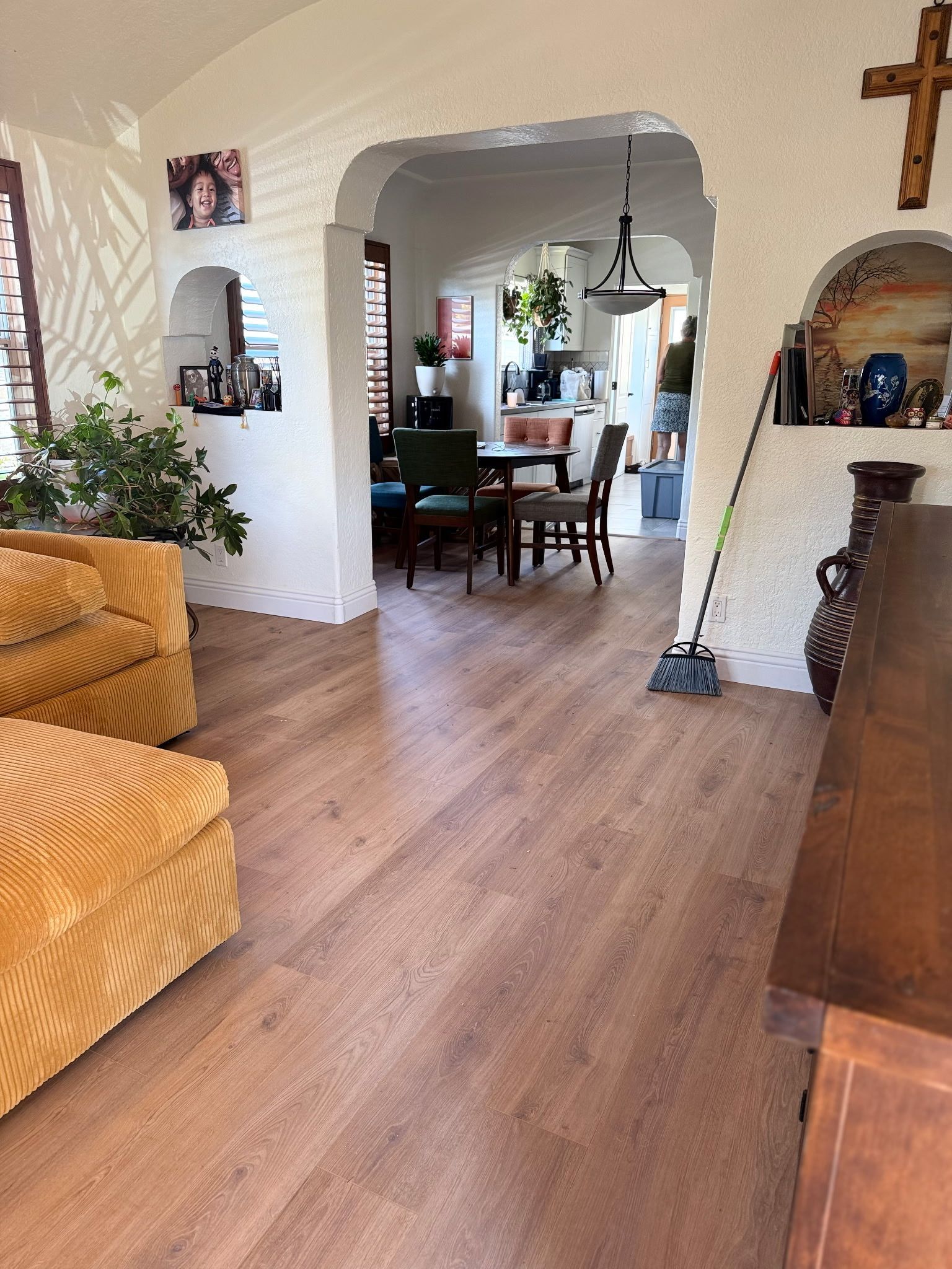 A view of a living room with yellow textured furniture and wood flooring, leading into a dining area through an archway.