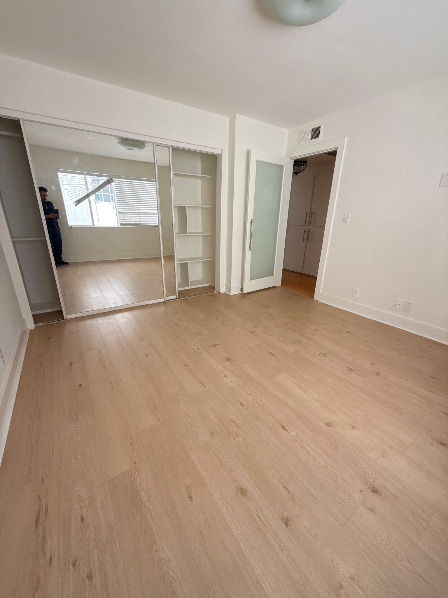An empty, bright room with light-toned wood flooring, a large mirrored closet, and two open doorways.