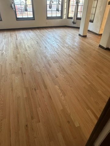 A room with light-colored hardwood flooring, white pillars, and large windows along the back wall.