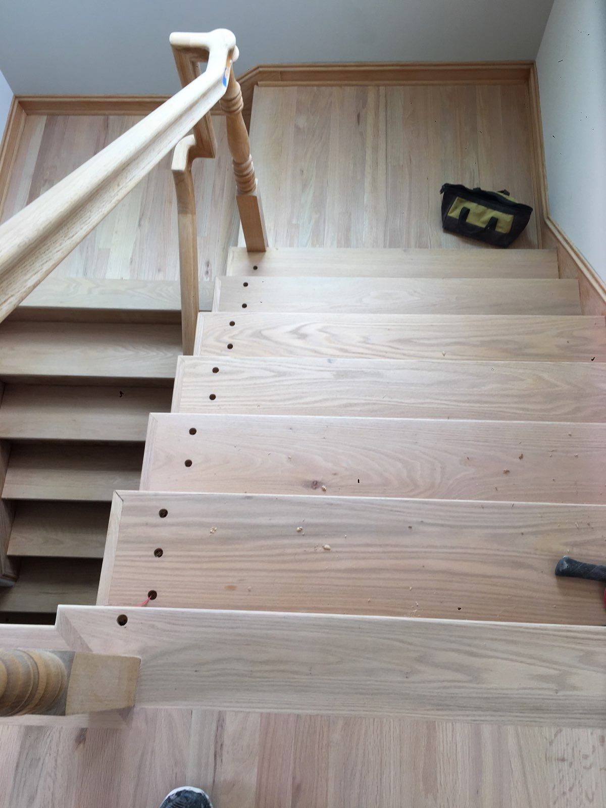 A high-angle view of wooden stairs under construction, featuring visible screw holes in the treads and a wooden handrail.