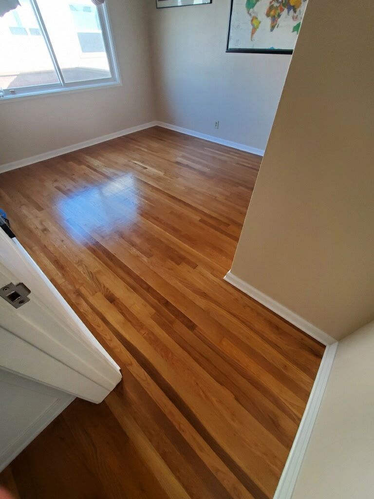 An empty room with polished hardwood floors, white baseboards, a window, and a world map on the wall.