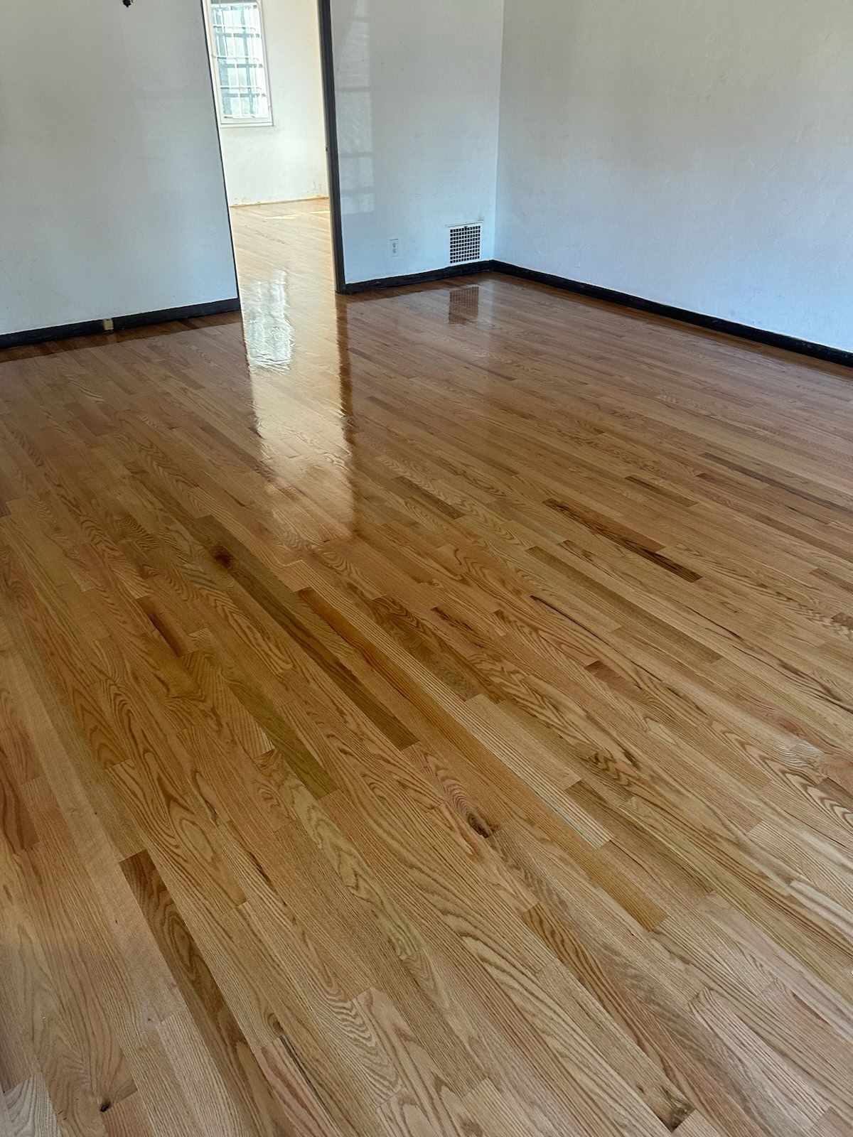 A room with glossy, light-brown hardwood flooring and a central vertical post against a white wall.