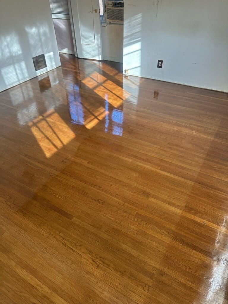 Polished, light-brown hardwood flooring in a room with white walls and a visible window light reflection.
