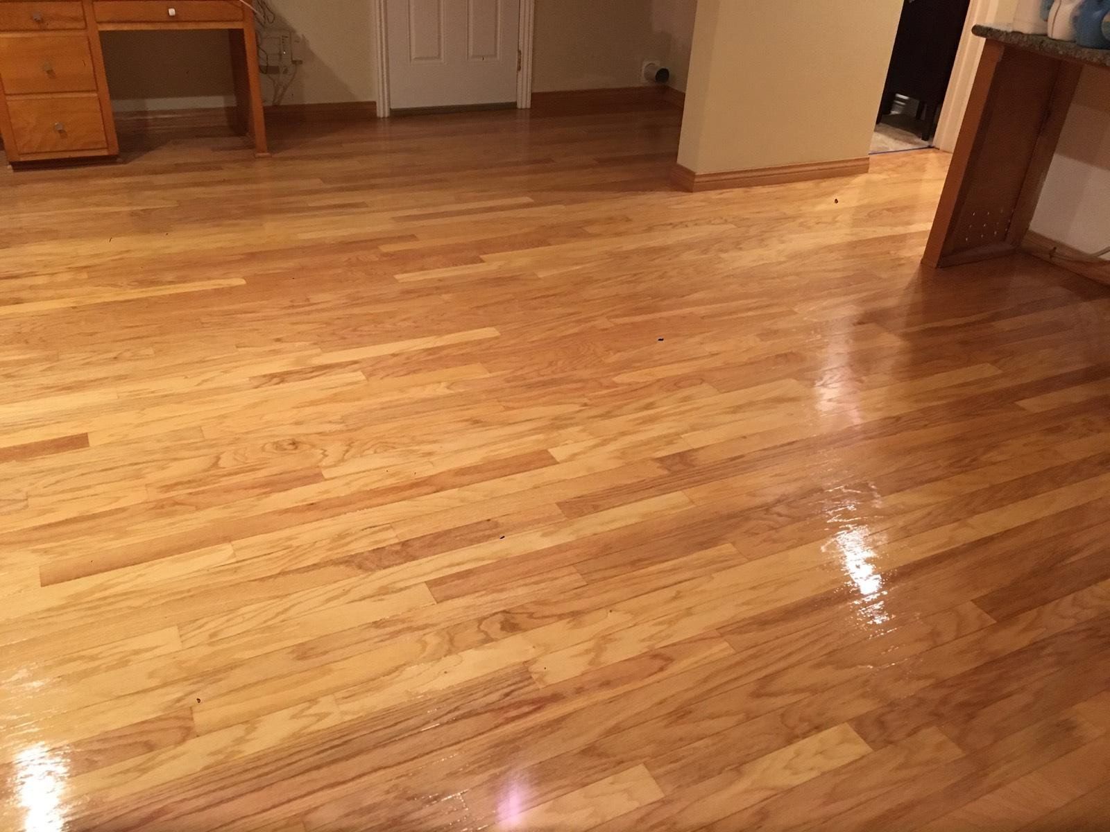 A polished hardwood floor in a room with light-colored walls, wooden furniture, and a closed white door.