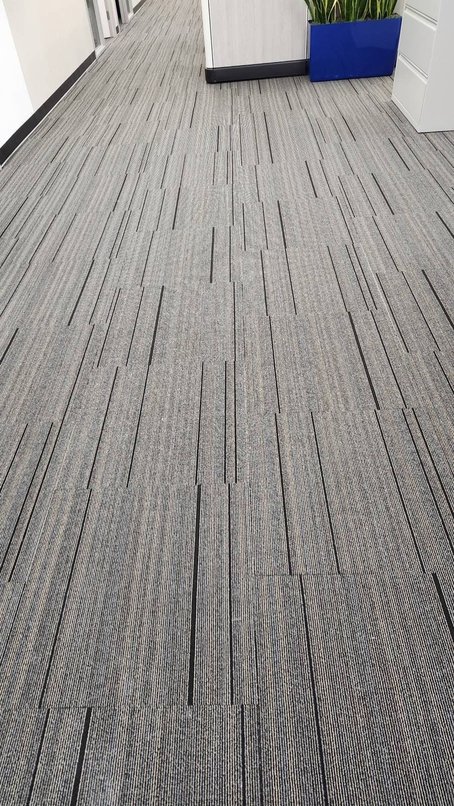 A hallway with carpet tiles featuring a black-and-white linear pattern that creates a swirling optical illusion.