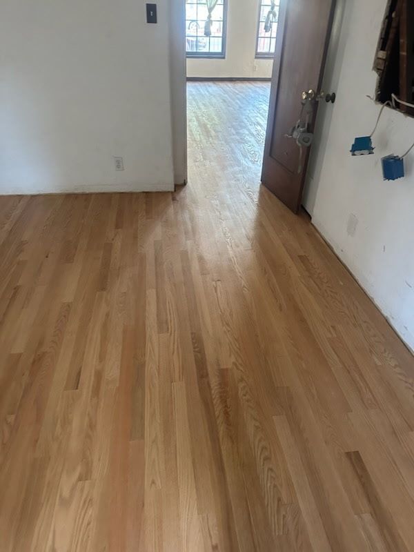 Newly installed light wood flooring in a room with white walls, leading through an open doorway into another room.