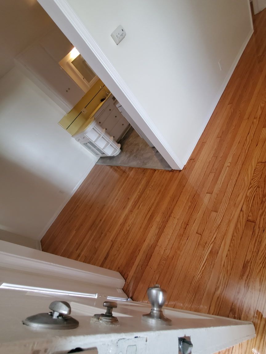 A view through an open doorway showing polished hardwood floors and a partial view of an adjacent room with a white dresser.