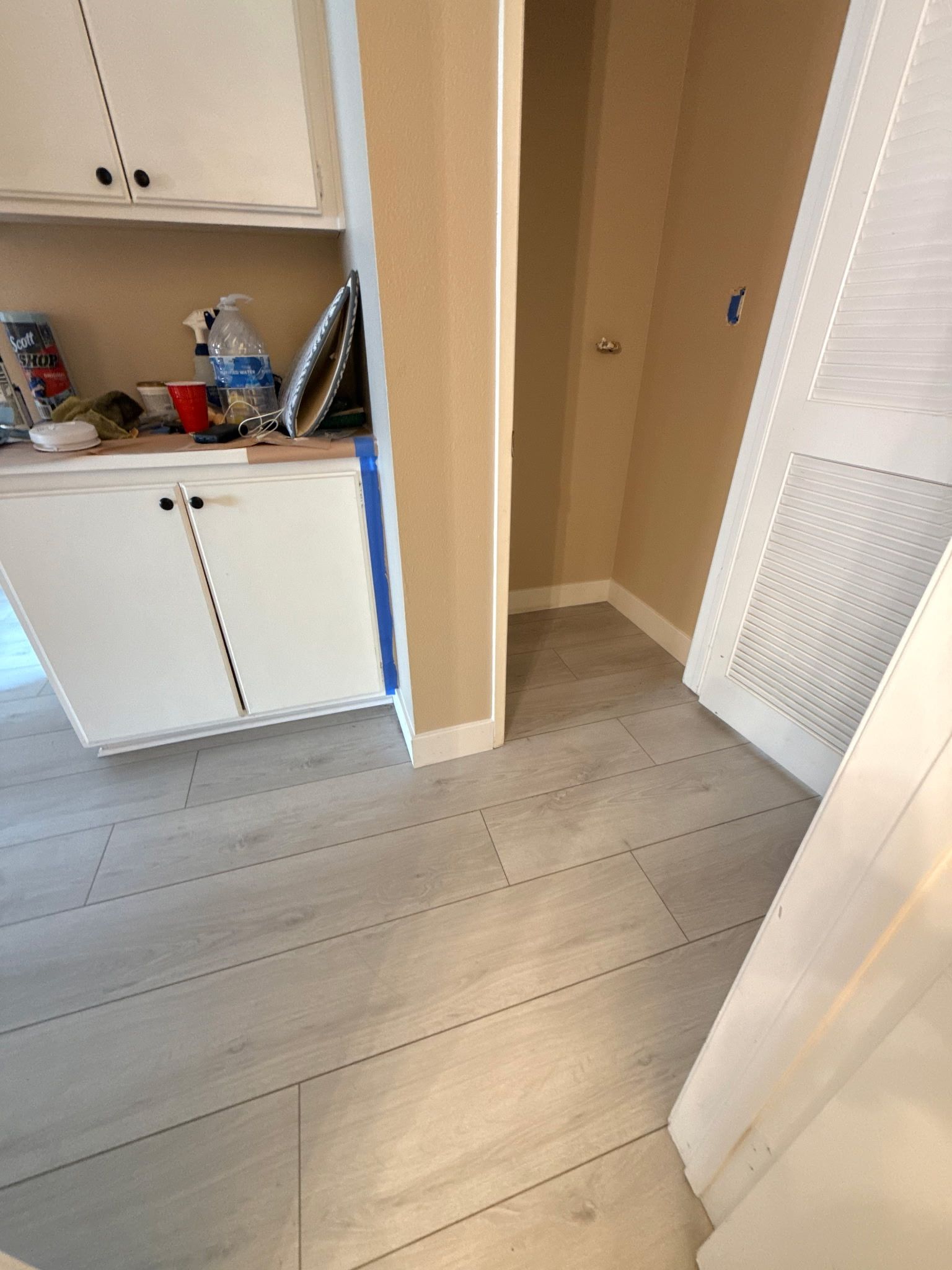 Light-colored wood flooring installed in a room with white cabinets and a beige-walled doorway.